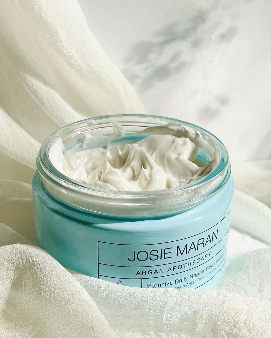 Josie Maran body butter in container on sheet