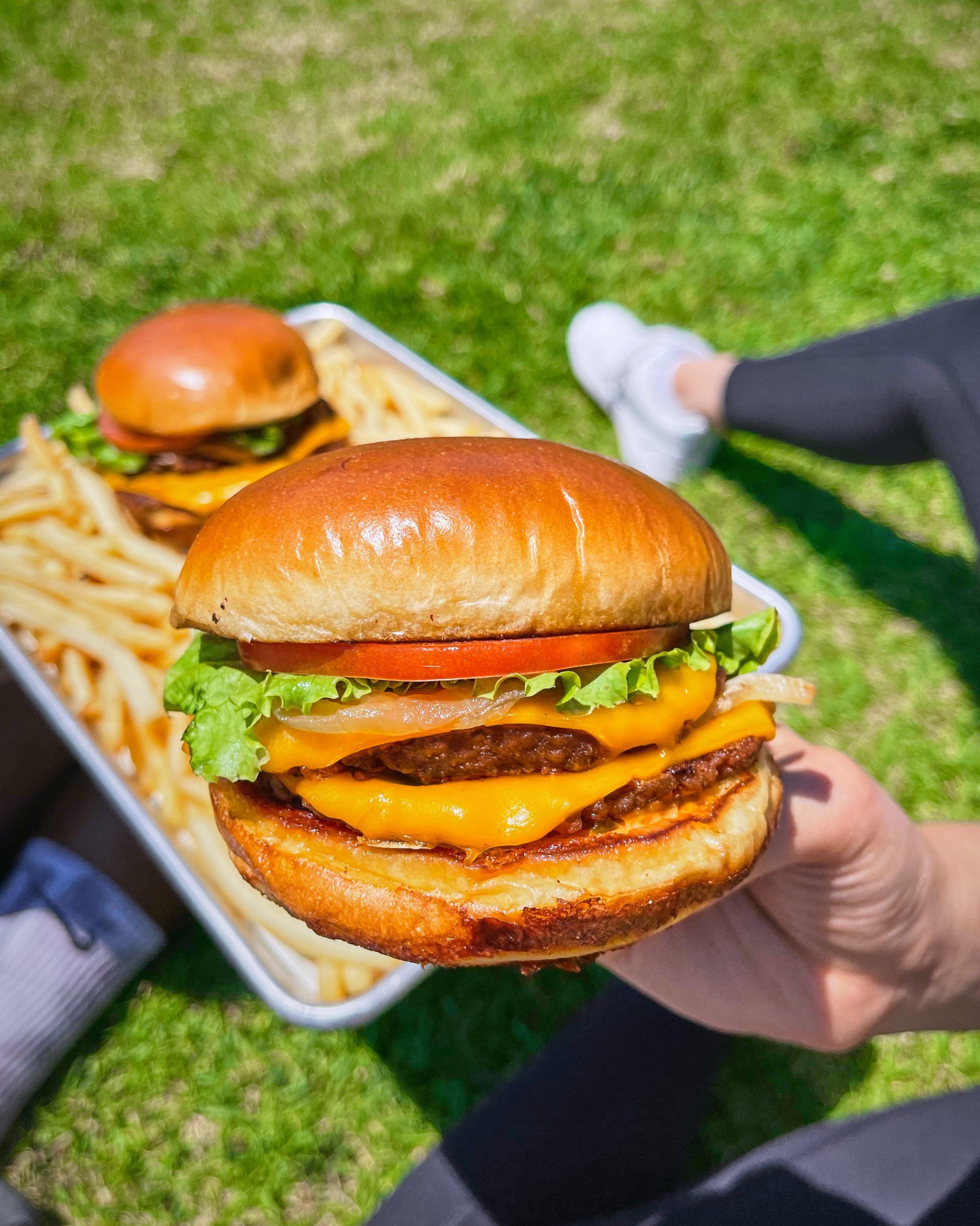 Person holding Hart House burger with meal on tray in the background