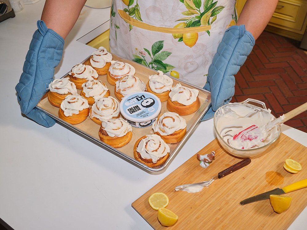 Person holding tray of cinnamon rolls with Oatly cream cheese on tray