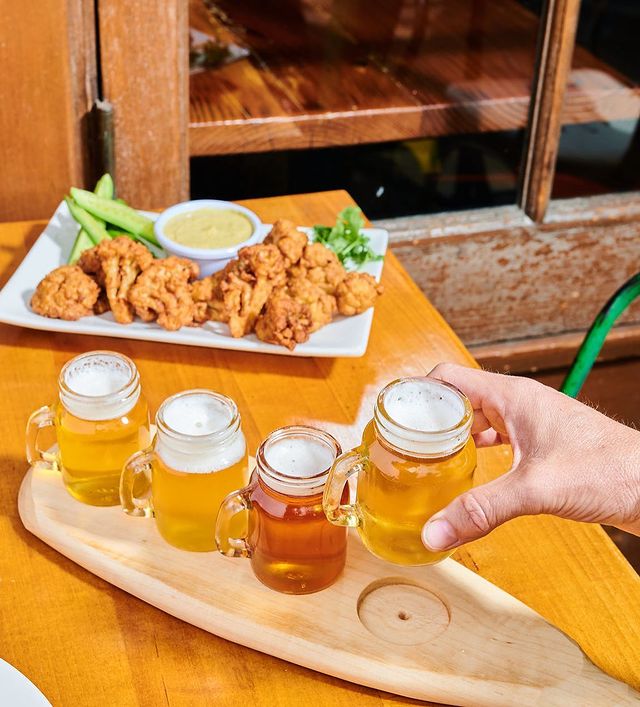 Person holding beer with food in background from Sage Plant Based Bistro & Brewery