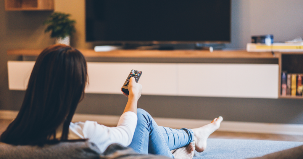 स्मार्टफोन पर स्क्रॉल करते हुए टीवी देखते हुए लोग