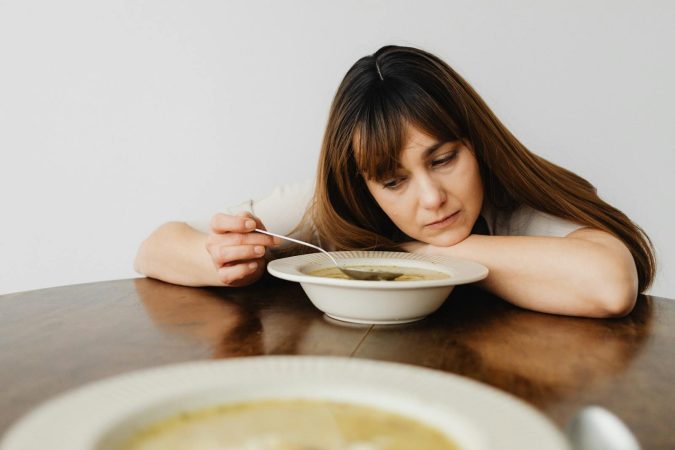 A woman sitting at a table looking contemplatively at her food, reflecting on her food choices