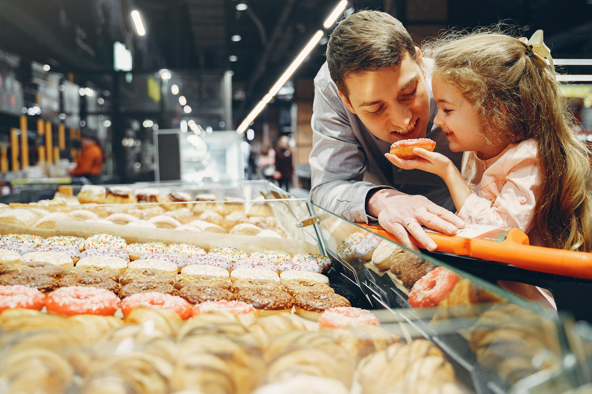 A father and daughter share a bonding moment choosing donuts at an indoor supermarket.