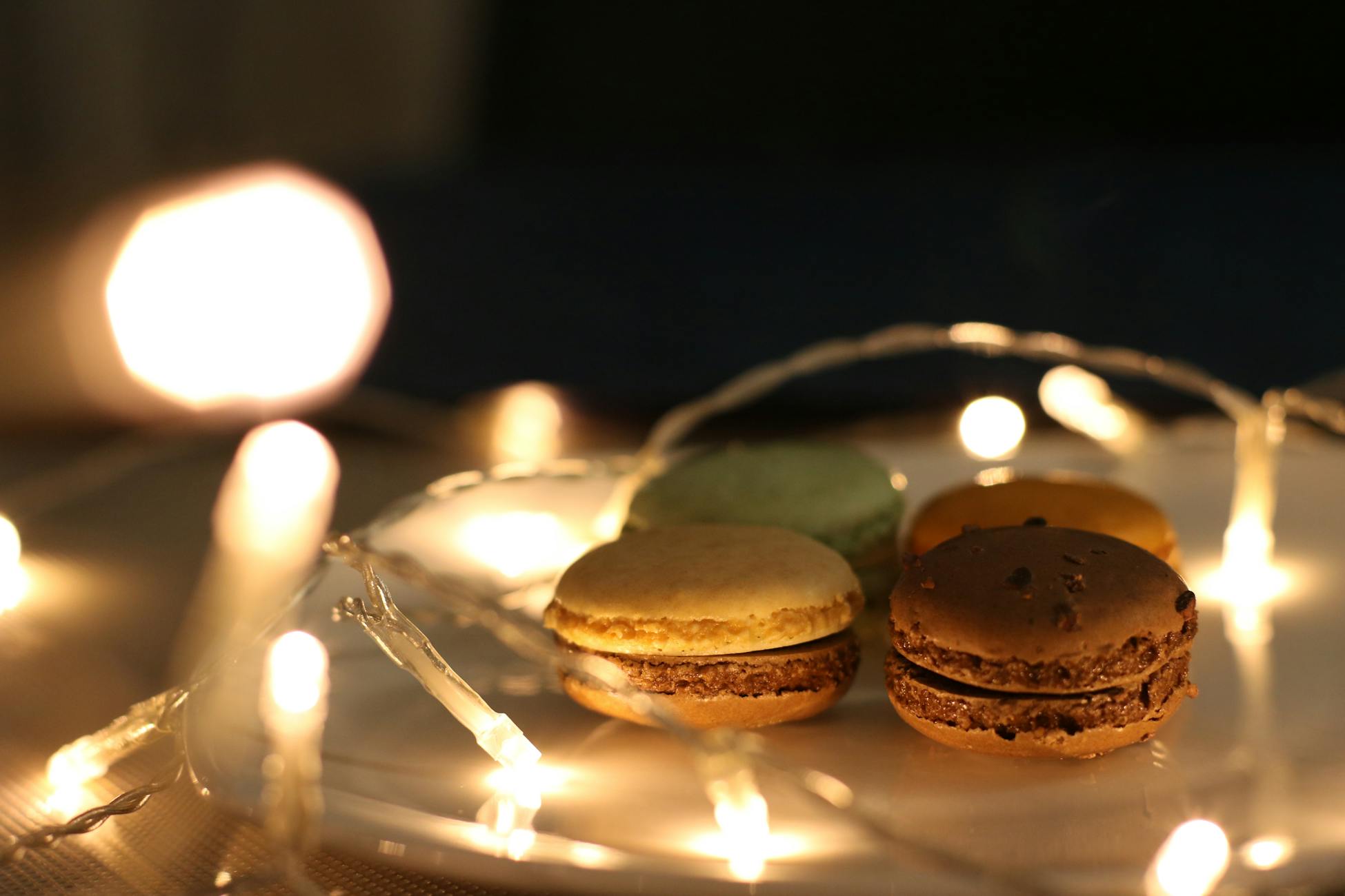 Delicious macarons on a plate illuminated by warm, glowing string lights for a festive feel.