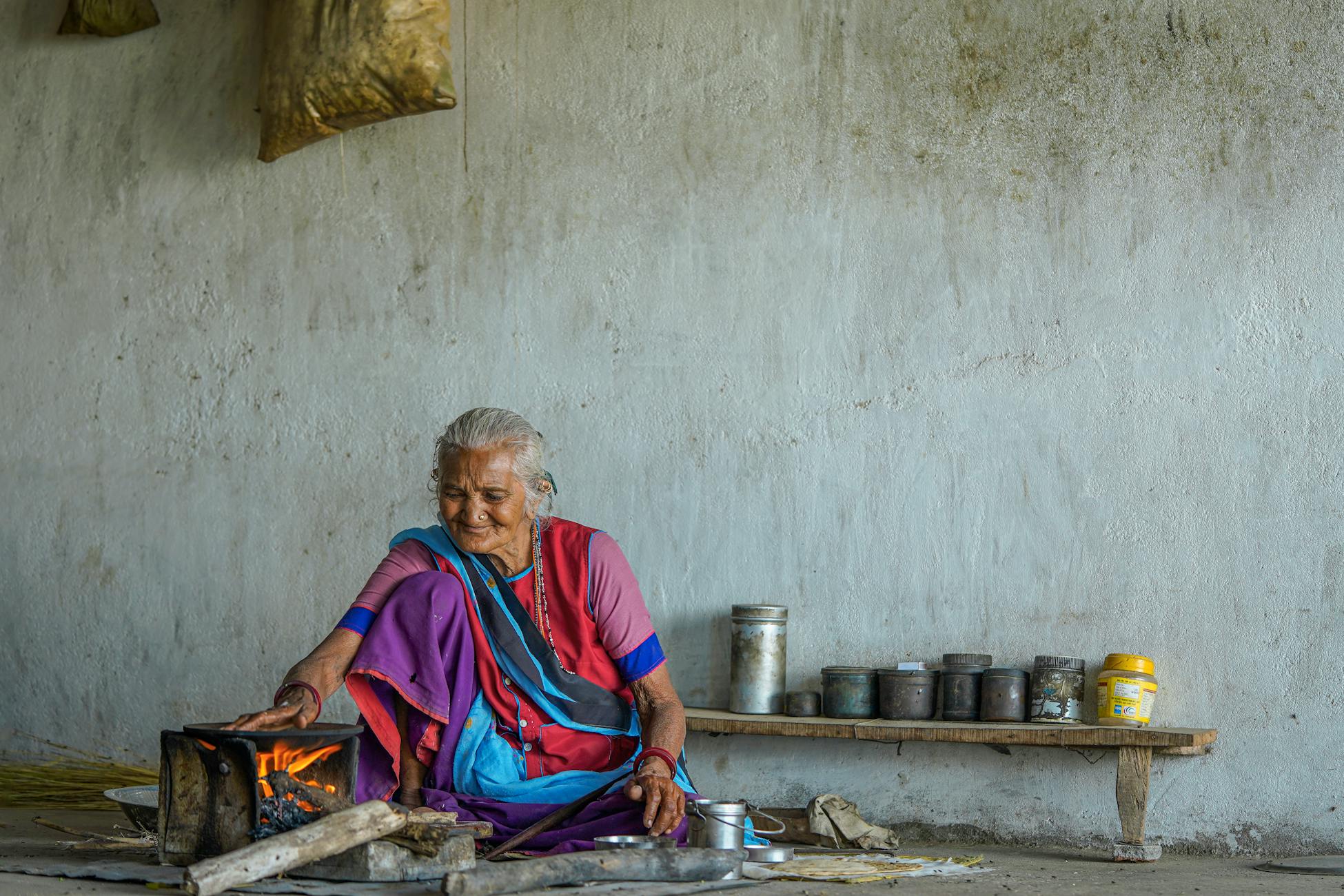 Senior Indian woman cooking with traditional fire in a rustic setting.