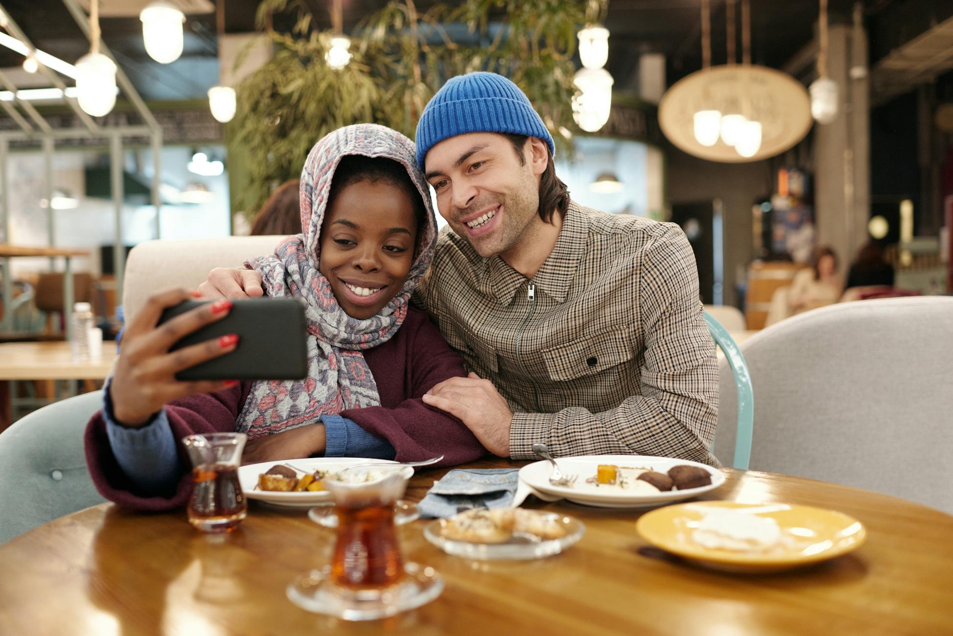 A joyful couple capturing a selfie in a cozy cafe while enjoying a meal together.