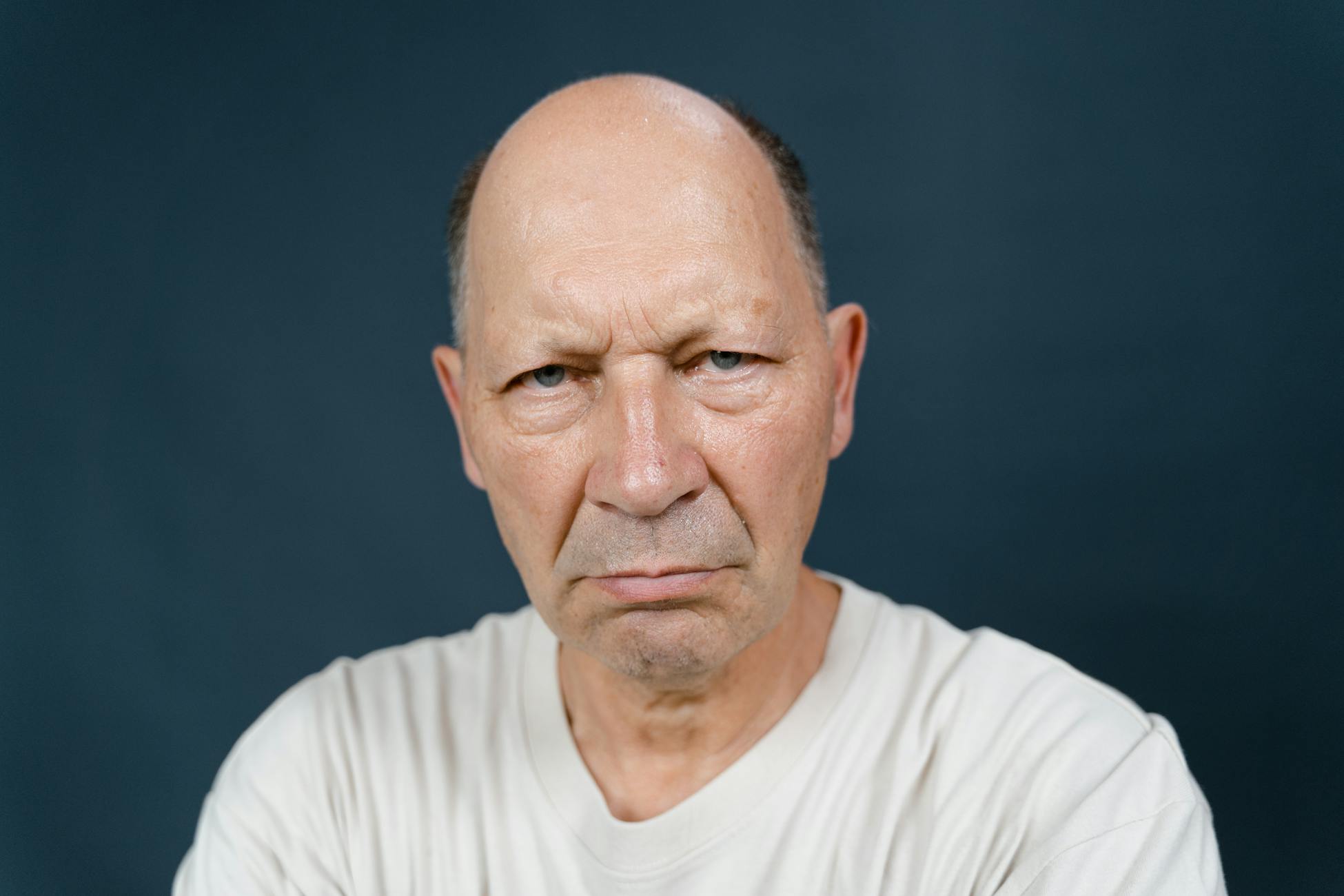Portrait of a serious senior man in a white shirt against a blue background.
