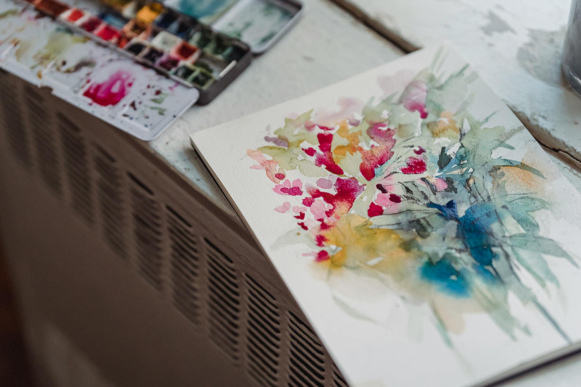 A vibrant floral watercolor painting on a sketchpad beside an artist's palette.