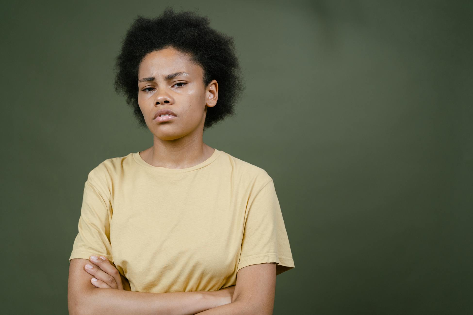 Expressive portrait of a woman with afro hair and yellow shirt against a green background.