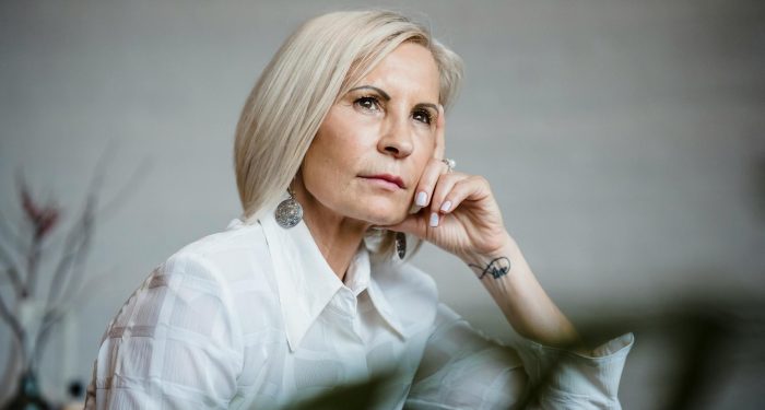 Portrait of a well-dressed senior woman lost in pensive thought indoors.