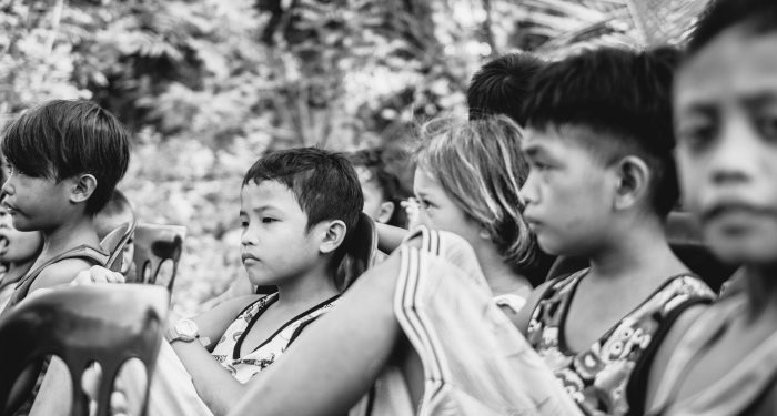 Black and white photo of children seated outside, displaying thoughtful expressions.