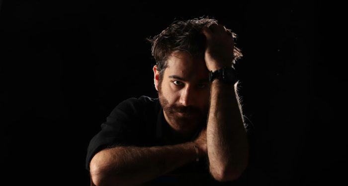 A contemplative man in a dark studio setting, captured in a dramatic and moody lighting.