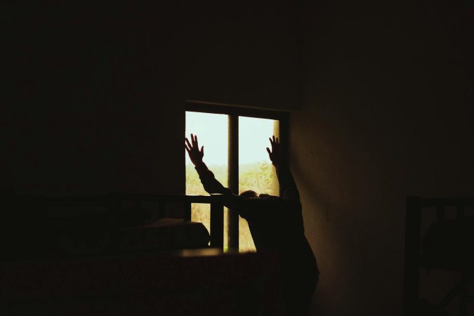 A silhouette of a man leaning against a window in a dimly lit room, creating a moody atmosphere.