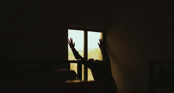 A silhouette of a man leaning against a window in a dimly lit room, creating a moody atmosphere.