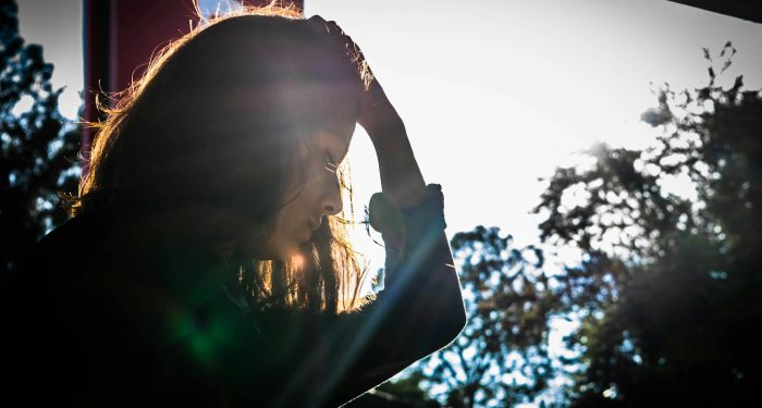 A silhouette of a woman touching her head, surrounded by nature and sunlight.