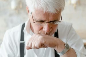 Elderly man with white hair and glasses deep in thought indoors.