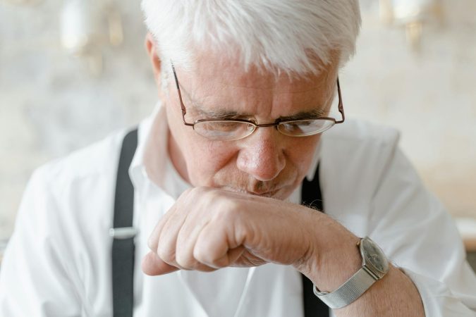 Elderly man with white hair and glasses deep in thought indoors.