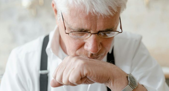 Elderly man with white hair and glasses deep in thought indoors.