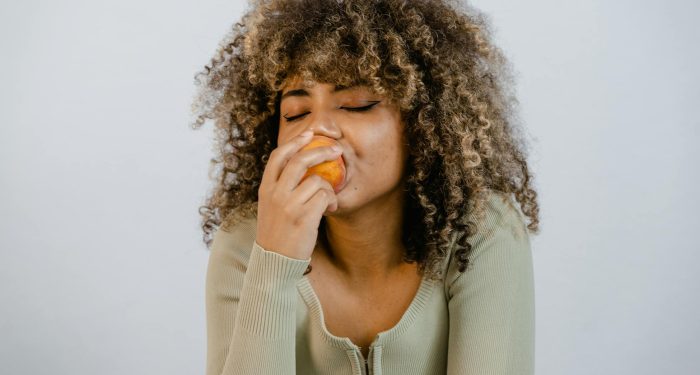 A woman with curly hair savors a peach, embodying a healthy lifestyle.