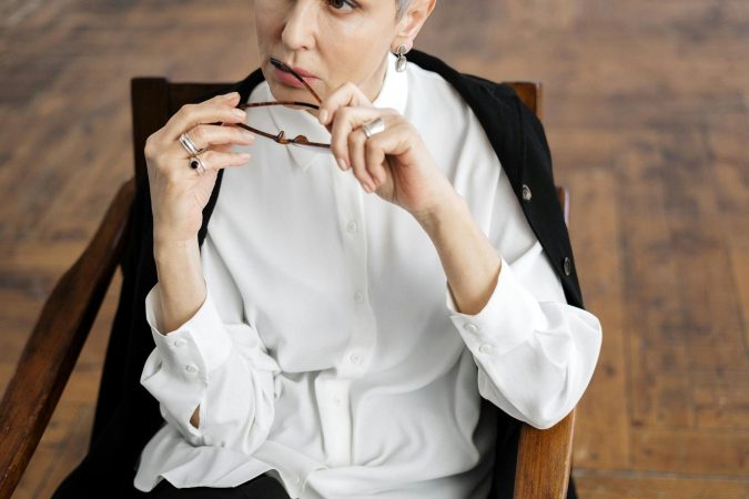 Woman in white shirt sitting thoughtfully holding glasses, symbolizing professional reflection.