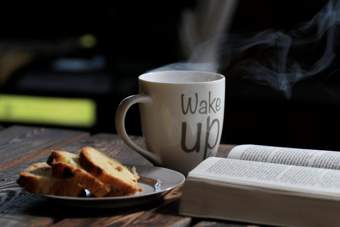 Steaming coffee with bread and an open book on a wooden table for a cozy morning.