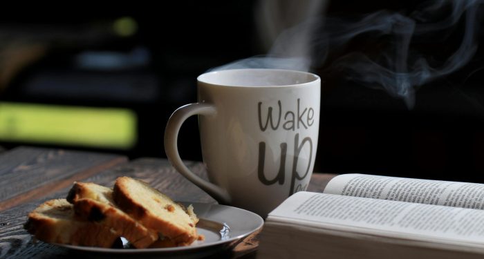 Steaming coffee with bread and an open book on a wooden table for a cozy morning.