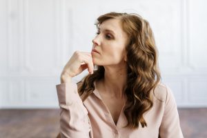 A thoughtful woman with curly hair sits indoors, reflecting deeply in a serene setting.