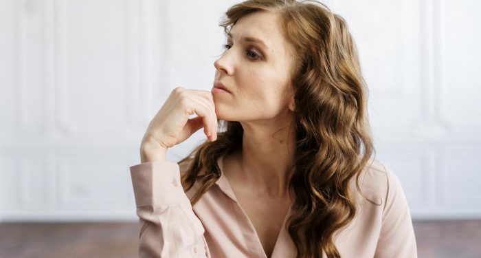A thoughtful woman with curly hair sits indoors, reflecting deeply in a serene setting.