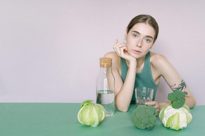 A young woman in a green top sitting with vegetables and a glass of water.