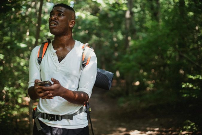 A hiker looks frustrated while using a smartphone to navigate in a dense forest.