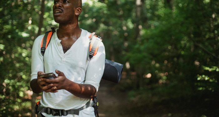 A hiker looks frustrated while using a smartphone to navigate in a dense forest.