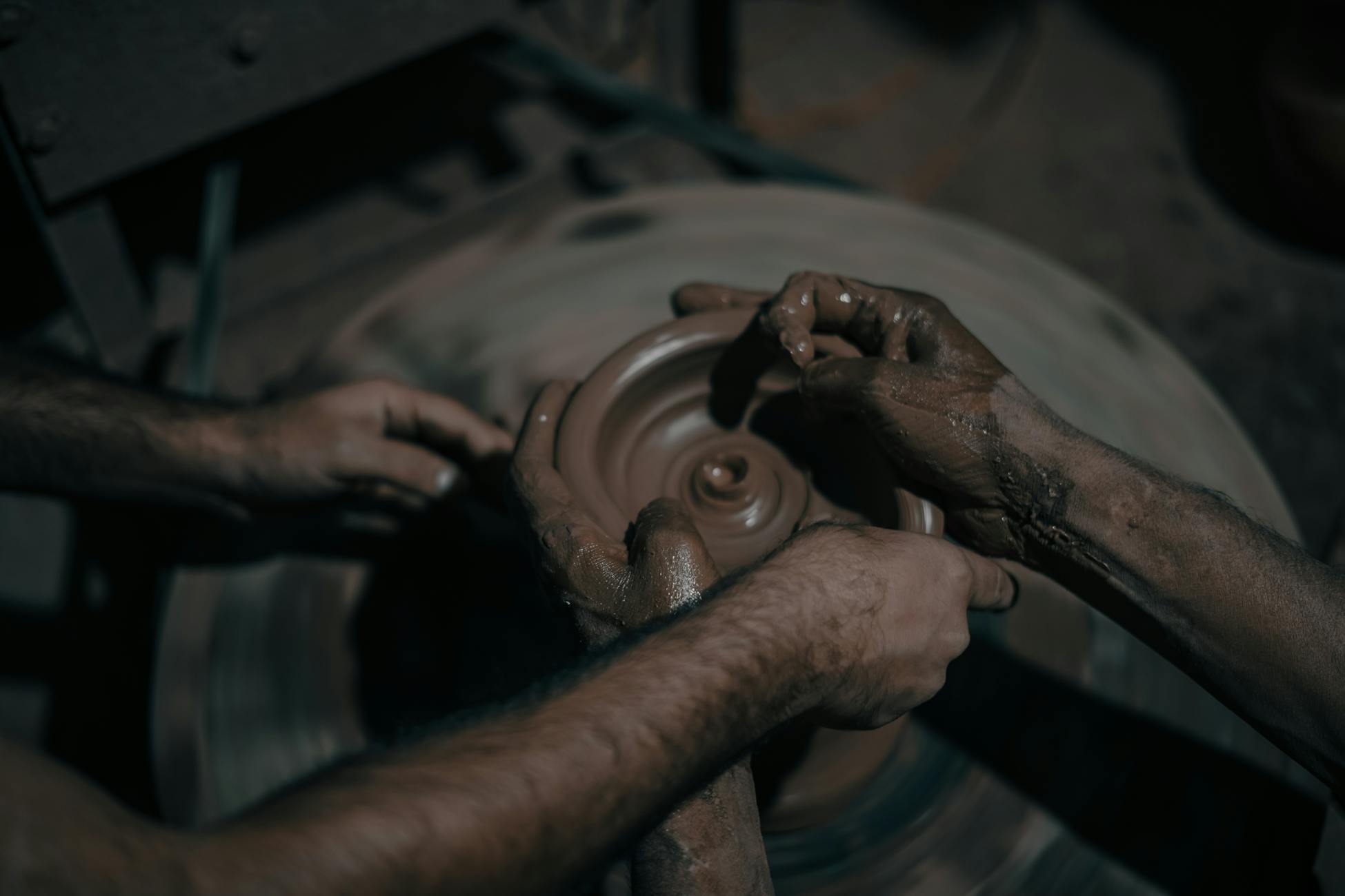 Artisan hands skillfully shaping clay on a pottery wheel in a workshop setting.