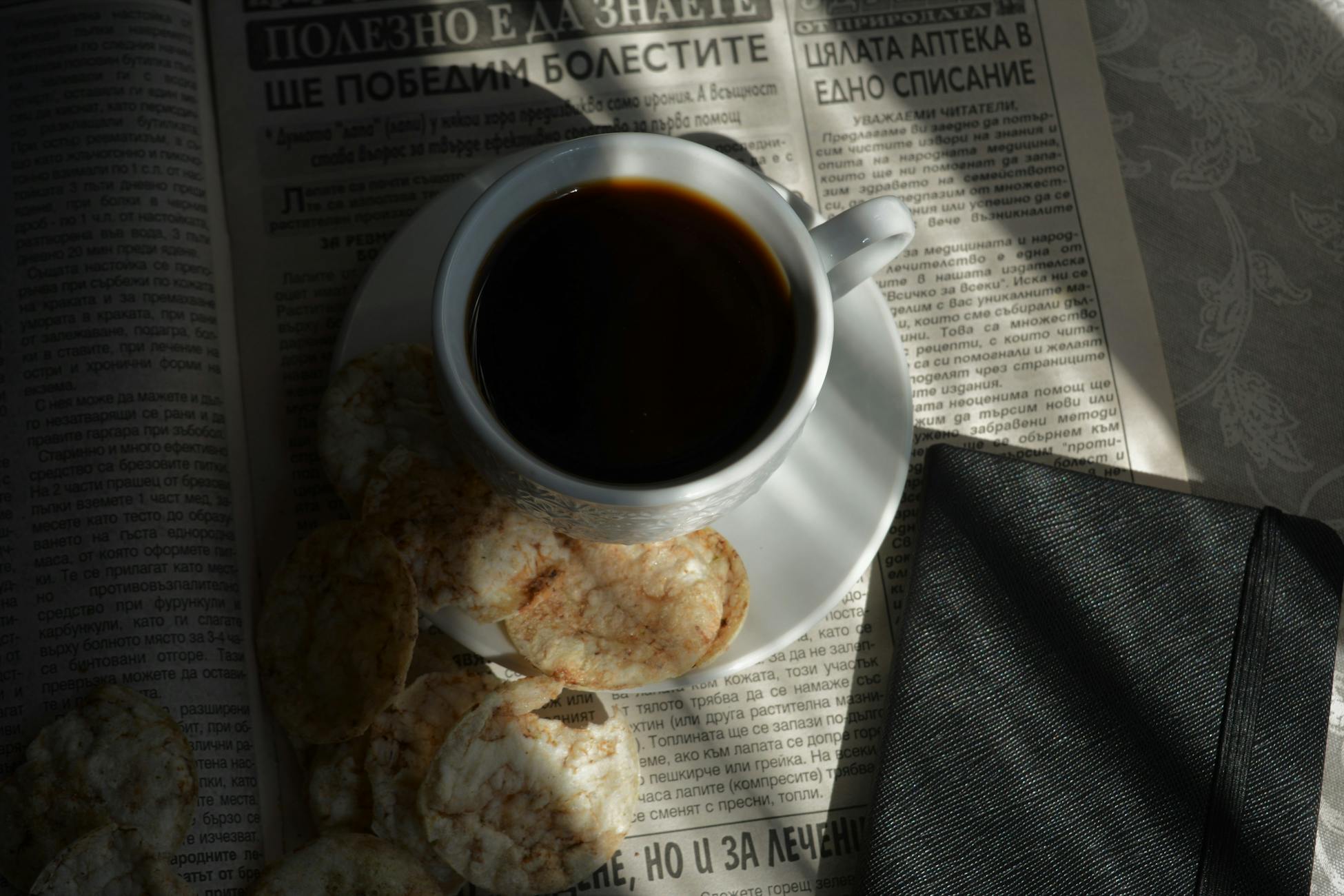 A cozy setup featuring a cup of black coffee, biscuits, and a newspaper, perfect for a relaxed morning.
