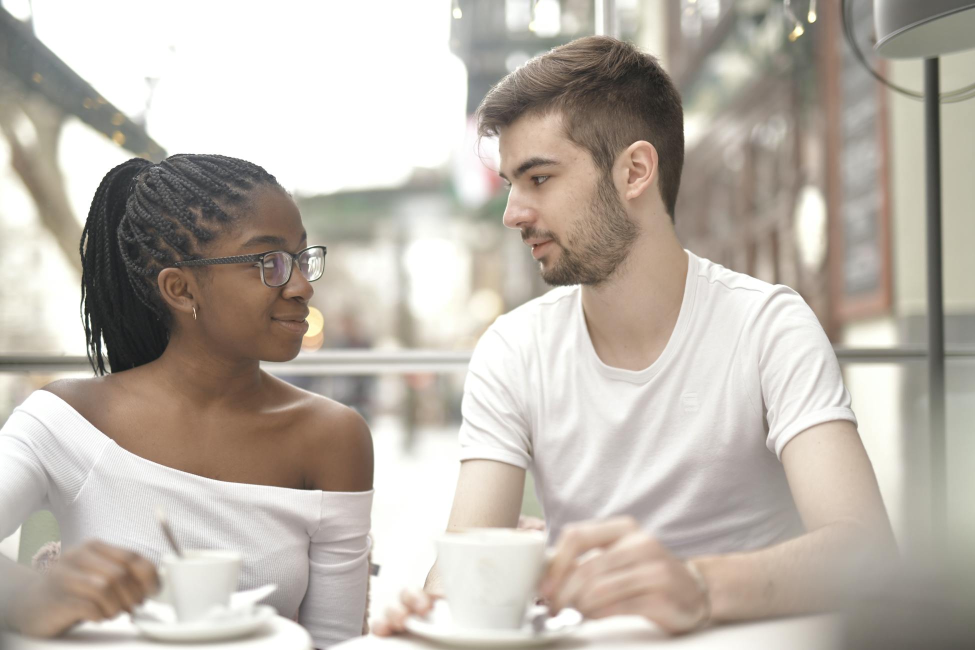 A multiracial couple enjoys coffee together in a bright café setting, sharing a warm moment.