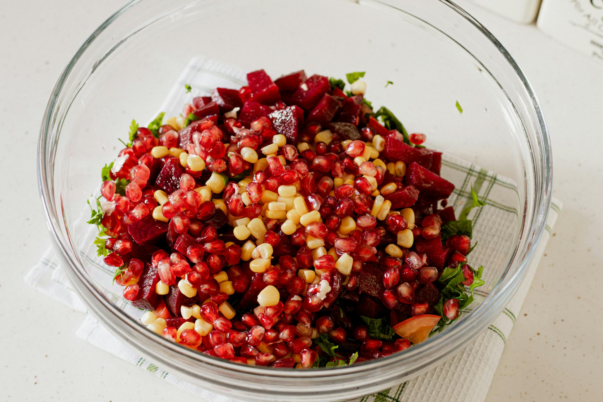 A fresh and colorful pomegranate beetroot salad with corn in a glass bowl indoors.