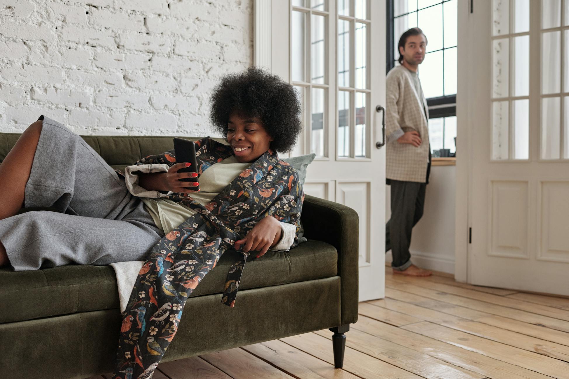 A couple relaxing at home, with a woman lying on the sofa using a smartphone.