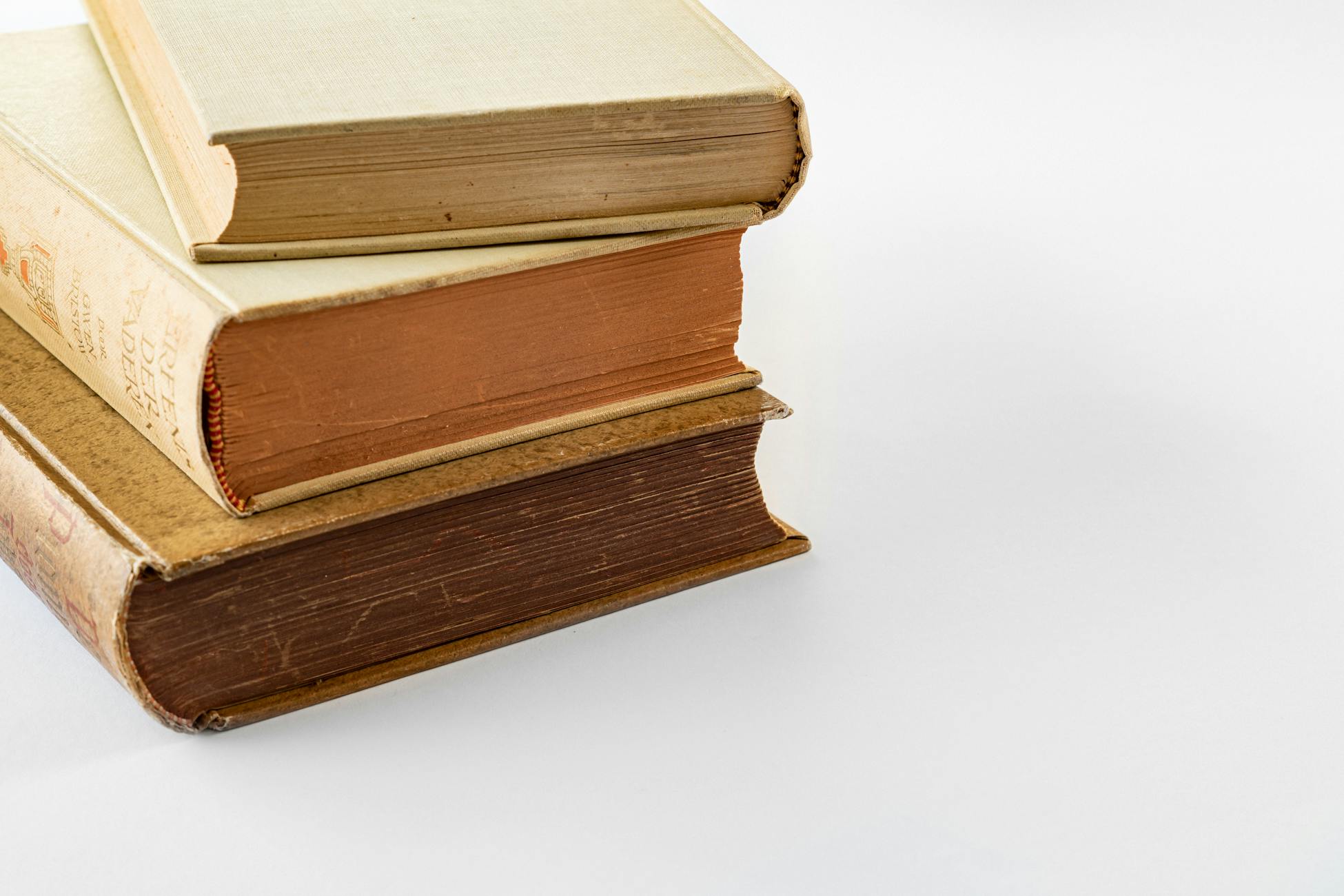 A close-up of three vintage hardbound books stacked on a white surface, showcasing their aged textures.