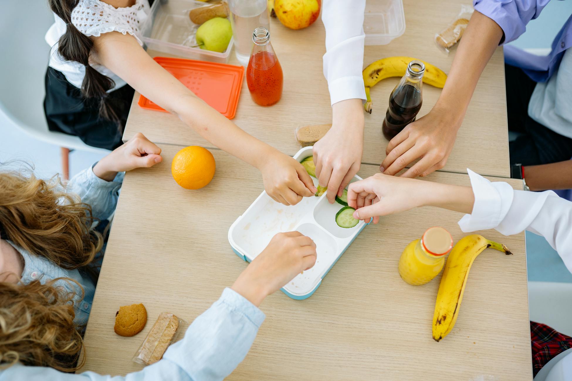 Children enjoying a variety of healthy snacks and drinks at a shared table, top view.