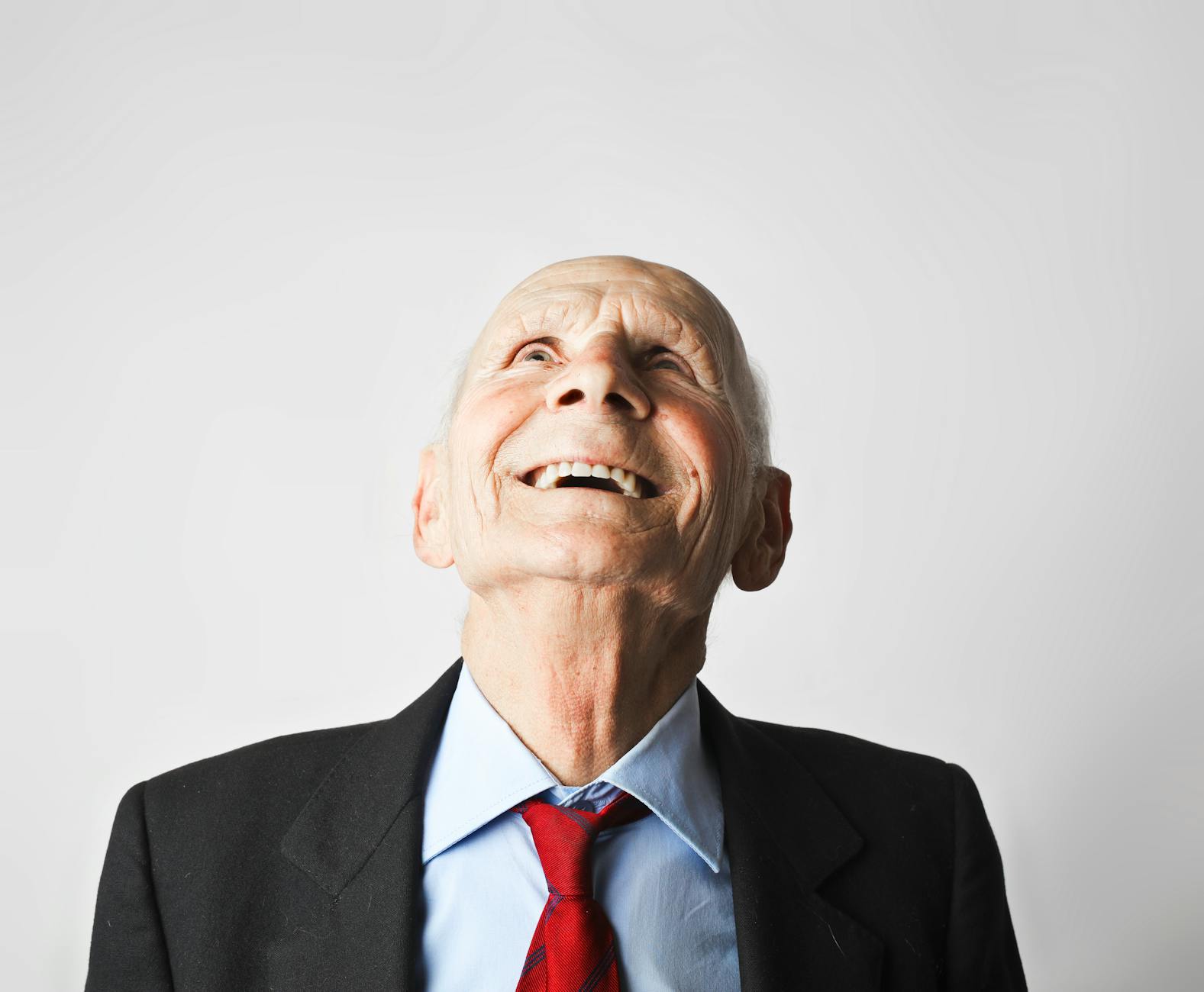 Smiling elderly man in formal attire looking up with happiness in a studio setting.