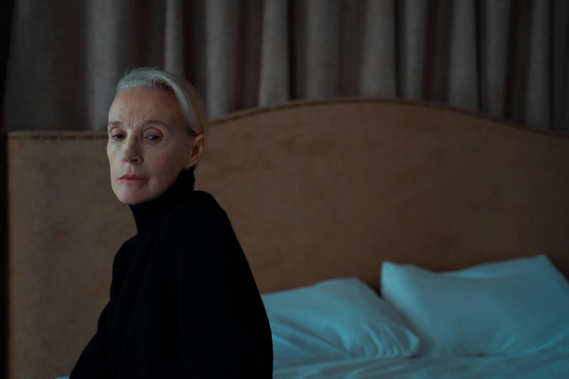 Senior woman in thoughtful solitude indoors on a bed.