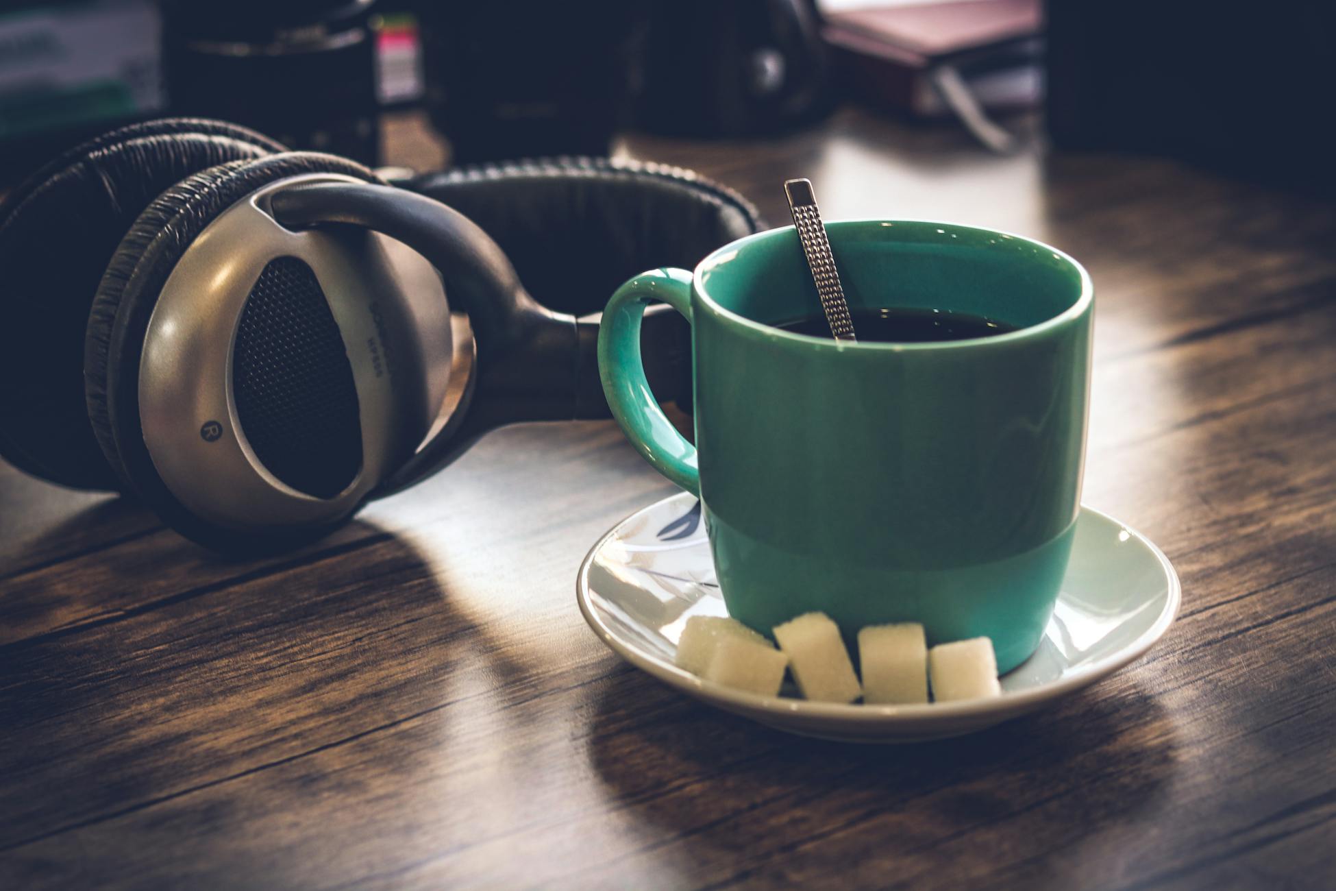 A cozy setup with a green coffee cup, sugar cubes, and headphones on a wooden table.