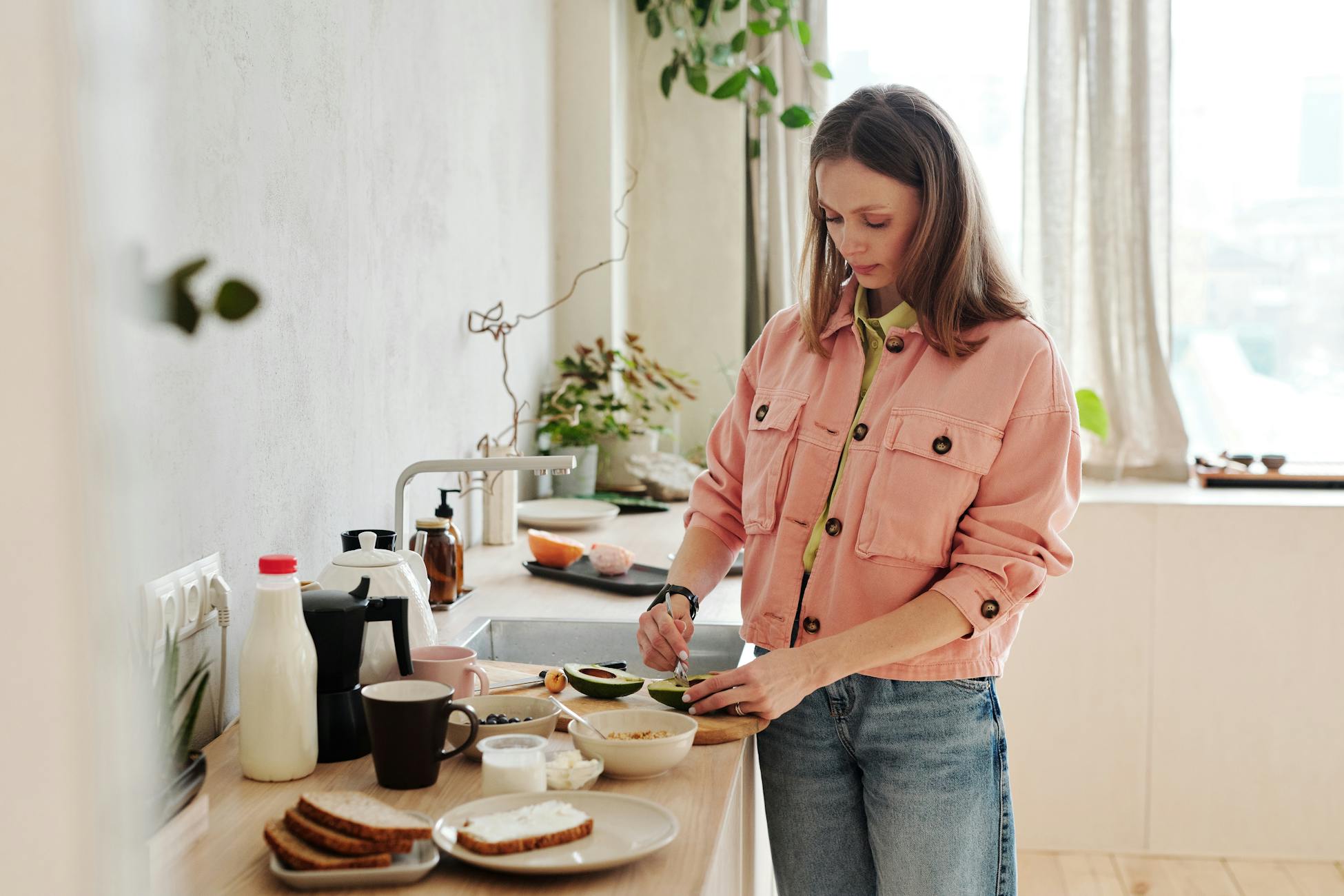 A woman slices an avocado in a bright, modern kitchen with natural light.