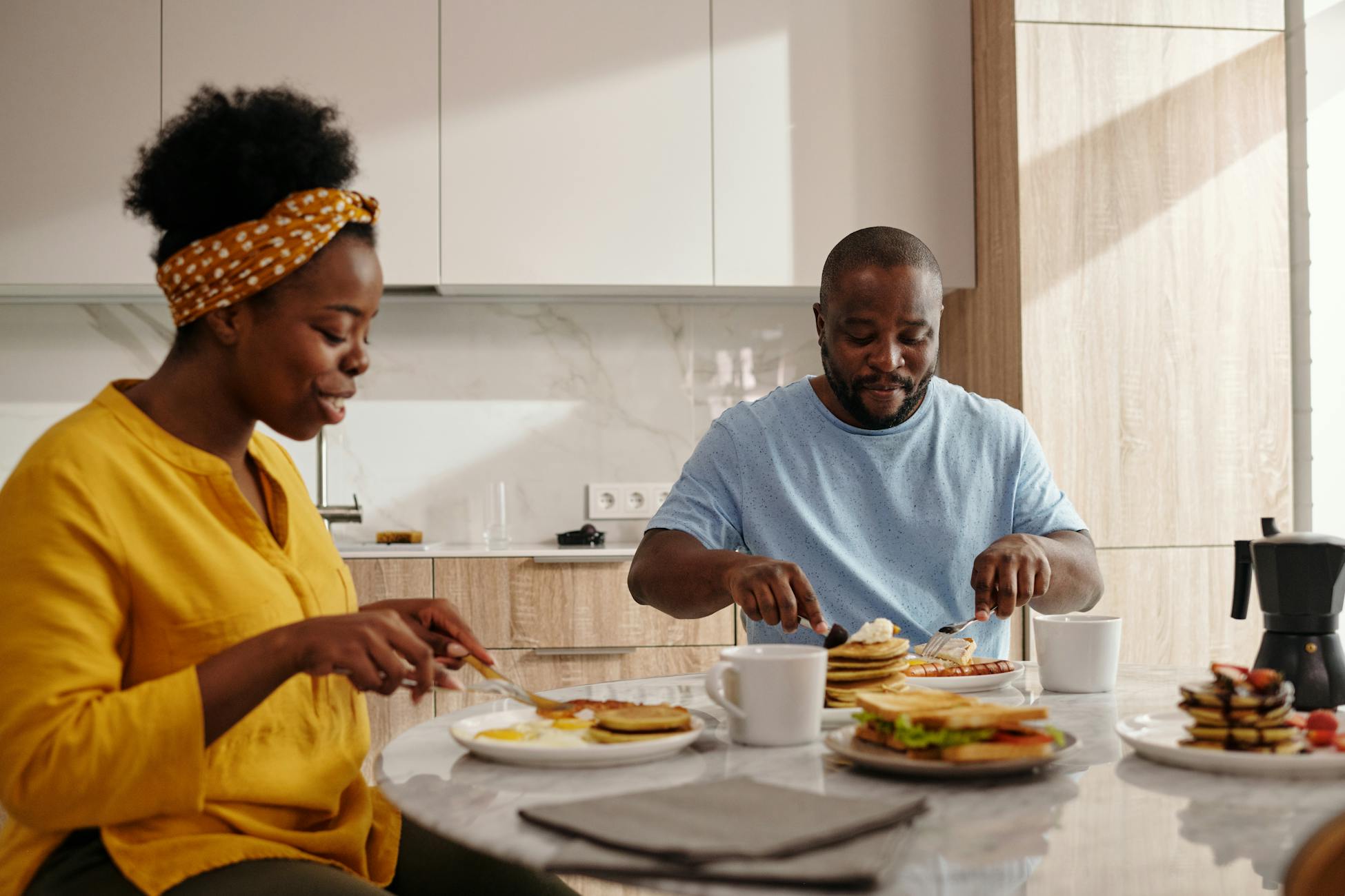 A joyful couple sharing a breakfast meal with pancakes, coffee, and smiles in their modern kitchen.