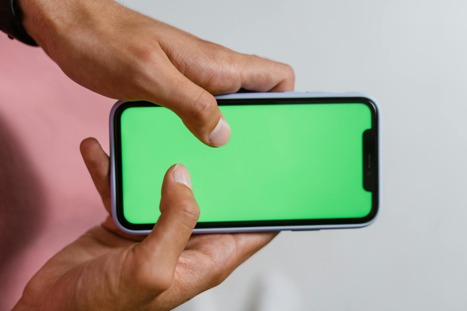 Hands holding smartphone with a green screen, suitable for digital content overlay.