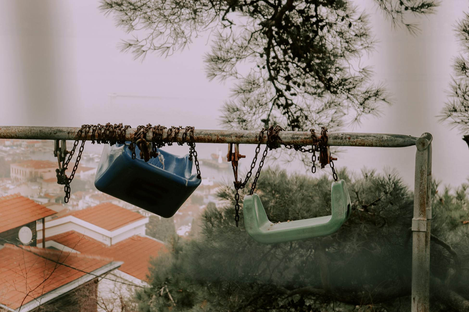 Outdoor scene of rusty swings with broken chains against a misty backdrop.
