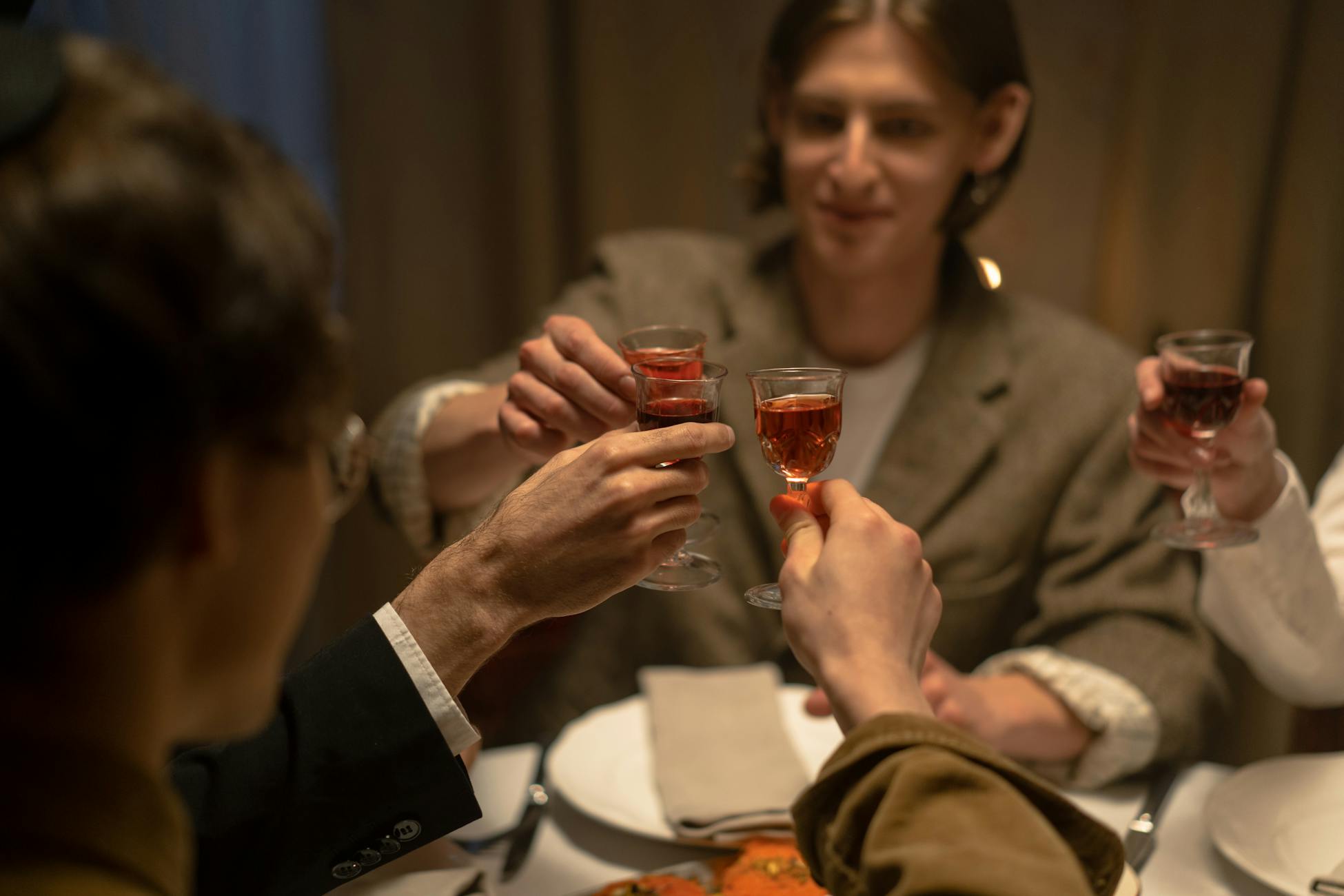 Adults toasting red wine around a dinner table in a Jewish celebration setting.