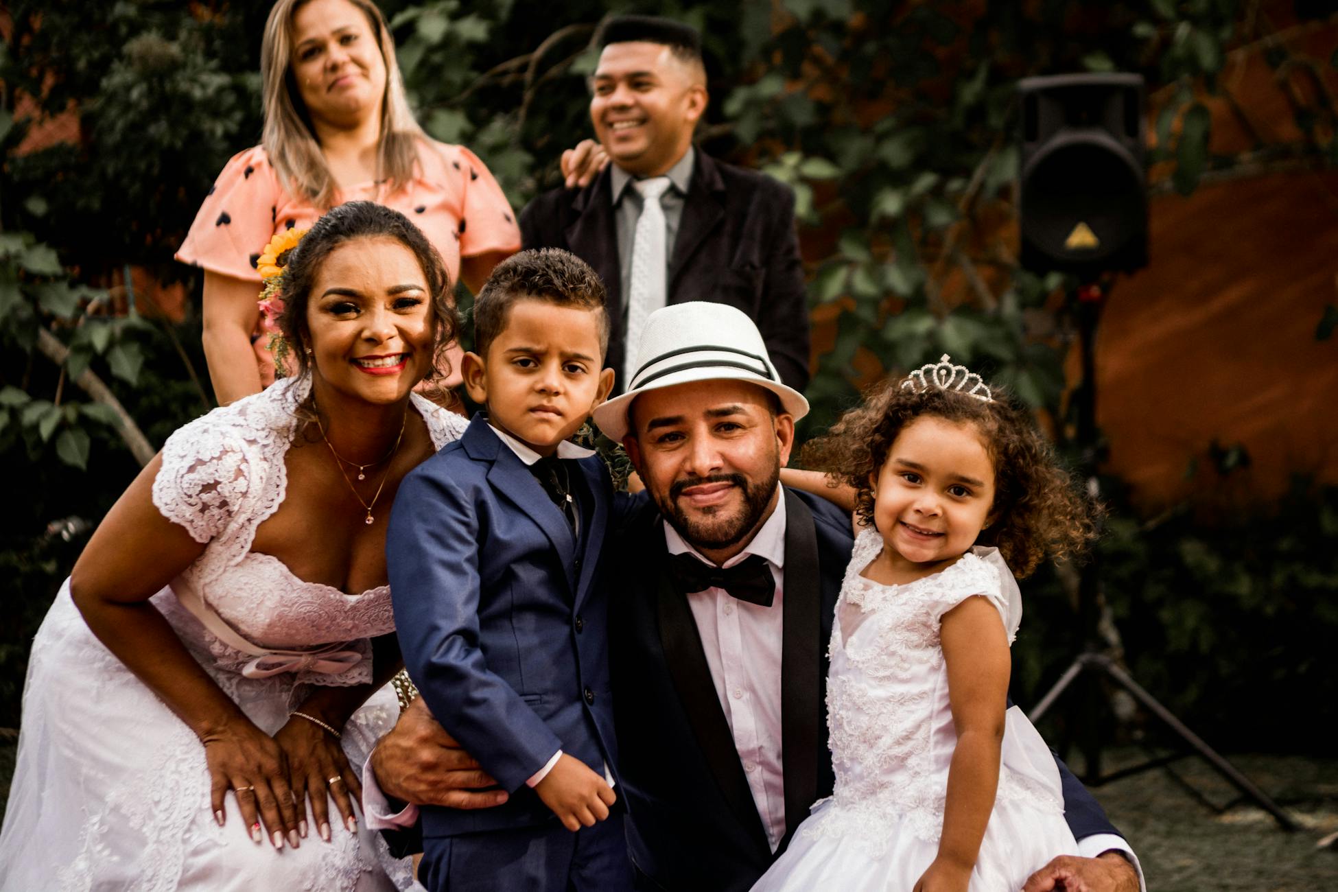 Joyful wedding celebration with family posing in elegant attire and natural setting.