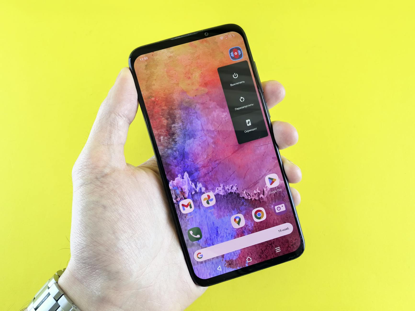 A close-up of a hand holding a smartphone with a colorful abstract wallpaper against a yellow background.