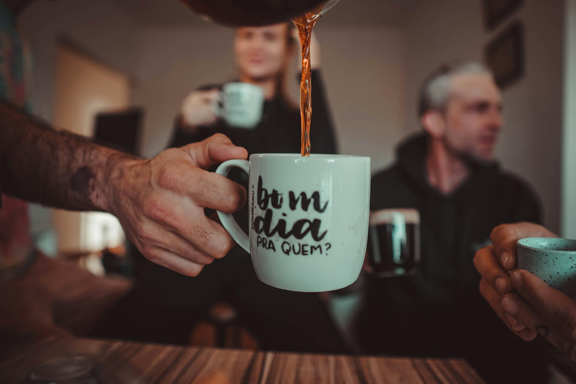 Three people enjoying coffee indoors with a humorous mug inscription.
