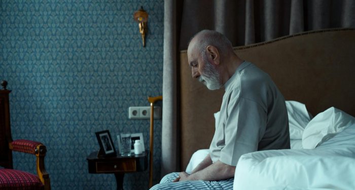 Elderly man sitting on bed, reflecting, in a cozy classic bedroom setting.